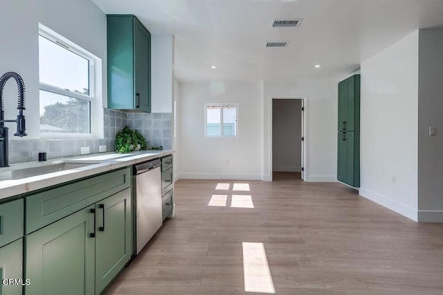 kitchen featuring decorative backsplash, light countertops, stainless steel dishwasher, green cabinets, and a sink