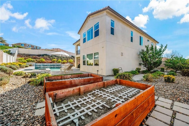 rear view of property with a garden, an outdoor pool, fence, a patio area, and stucco siding