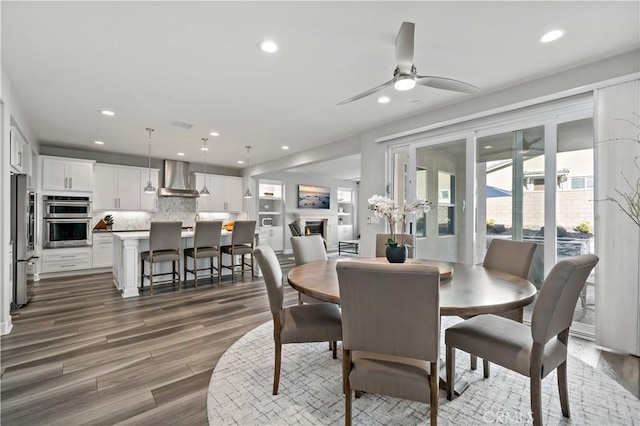 dining area with a lit fireplace, ceiling fan, wood finished floors, and recessed lighting