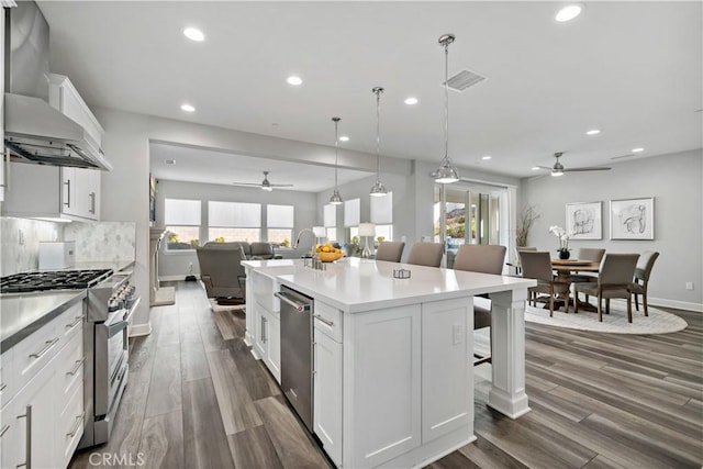 kitchen with a breakfast bar area, stainless steel appliances, decorative backsplash, open floor plan, and wall chimney range hood