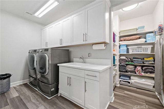 laundry room with cabinet space, visible vents, a sink, wood finished floors, and independent washer and dryer