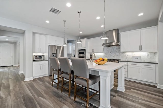 kitchen with visible vents, a kitchen breakfast bar, stainless steel appliances, wall chimney range hood, and backsplash