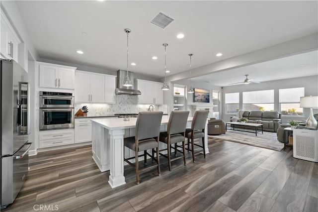 kitchen with a kitchen island with sink, visible vents, wall chimney range hood, appliances with stainless steel finishes, and tasteful backsplash