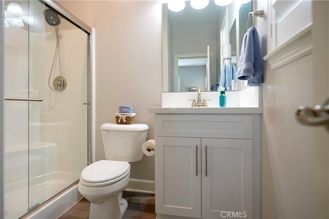 bathroom with toilet, a shower stall, vanity, wood finished floors, and baseboards