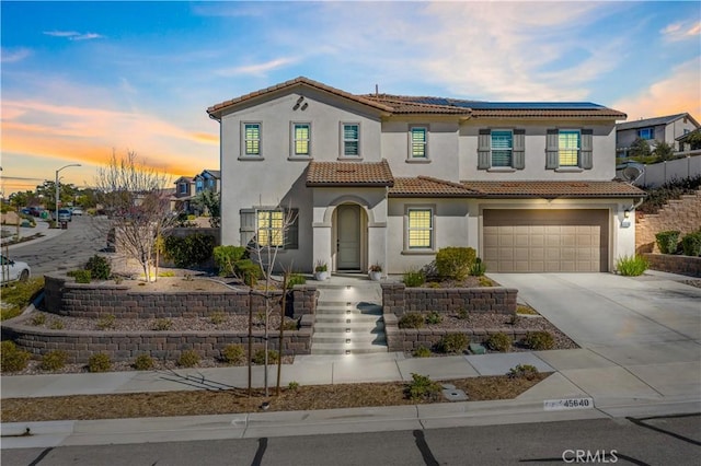 mediterranean / spanish home featuring concrete driveway, an attached garage, a tiled roof, and stucco siding