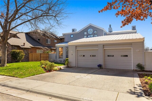 traditional-style house featuring fence, a front lawn, an attached garage, driveway, and metal roof
