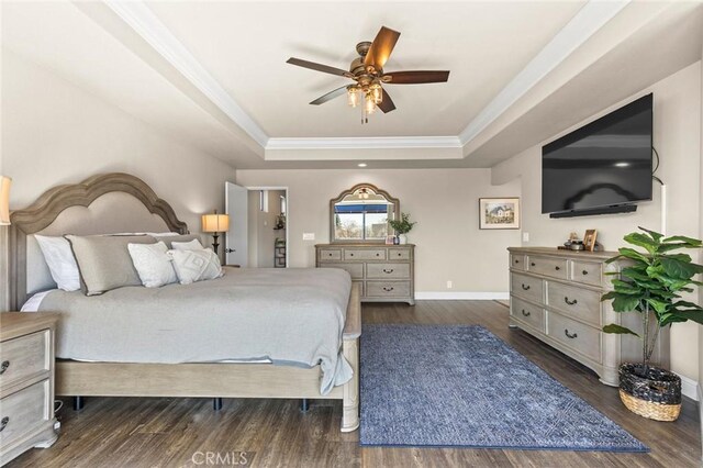 bedroom featuring a tray ceiling, wood finished floors, baseboards, and ornamental molding