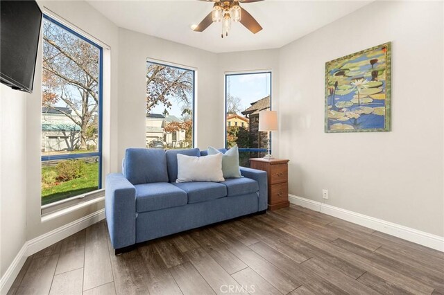 living area featuring wood finished floors, baseboards, and ceiling fan