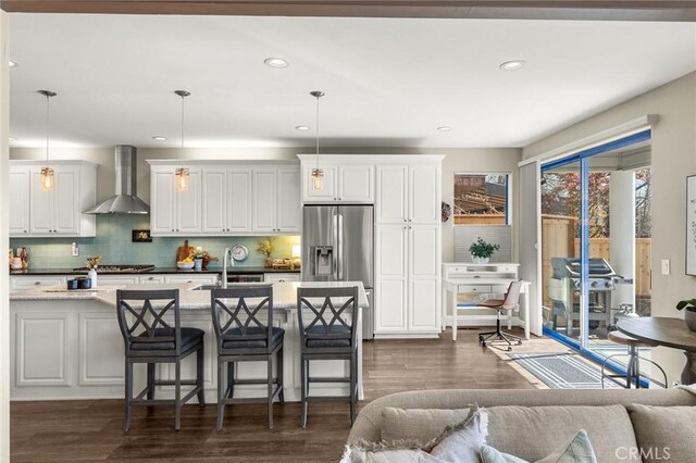 kitchen with a kitchen breakfast bar, wall chimney range hood, dark wood-type flooring, tasteful backsplash, and appliances with stainless steel finishes