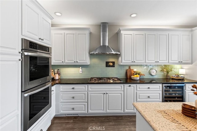 kitchen with beverage cooler, wall chimney range hood, appliances with stainless steel finishes, and white cabinets