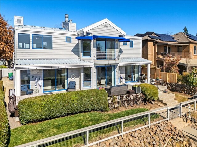 rear view of house with a balcony, a chimney, a fenced backyard, a patio, and metal roof