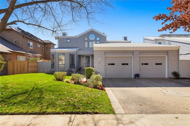 traditional-style house with driveway, an attached garage, fence, a front yard, and metal roof