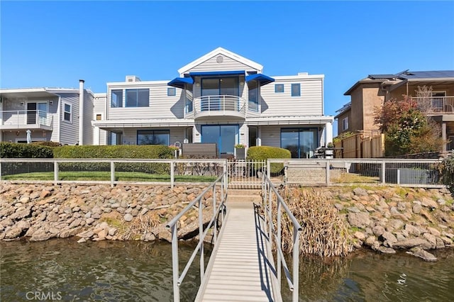 dock area with a water view, fence, and a balcony