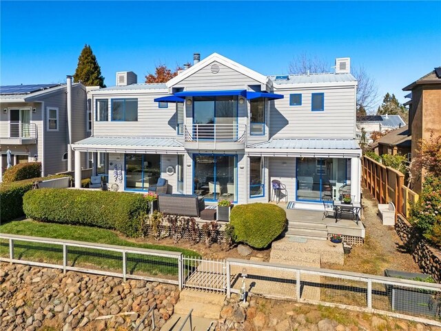 rear view of property featuring a chimney, a fenced front yard, a balcony, a patio area, and metal roof