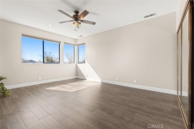 spare room featuring ceiling fan, dark wood-type flooring, visible vents, and baseboards