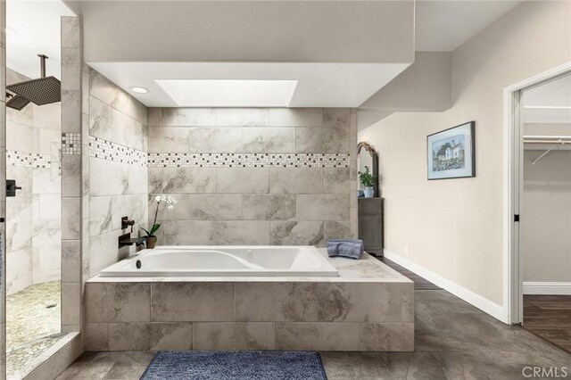 full bathroom featuring a skylight, a garden tub, walk in shower, and baseboards
