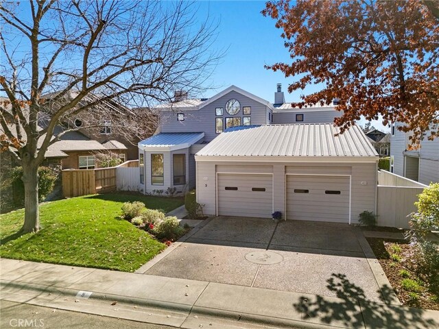 view of front facade featuring concrete driveway, a front lawn, an attached garage, fence, and metal roof