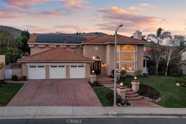 mediterranean / spanish house with a garage, solar panels, decorative driveway, stucco siding, and a front yard