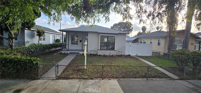 bungalow featuring a fenced front yard, a gate, a front lawn, and stucco siding