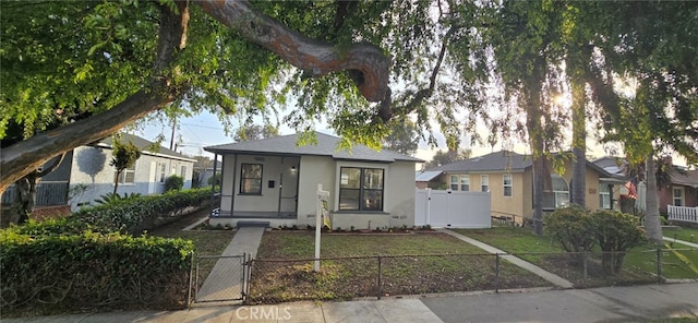 bungalow with a front lawn, a fenced front yard, a gate, and stucco siding