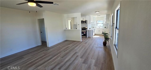 unfurnished living room with dark wood-type flooring, a ceiling fan, visible vents, and baseboards