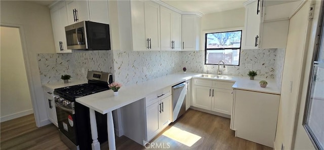 kitchen featuring wood finished floors, light countertops, stainless steel appliances, white cabinetry, and a sink