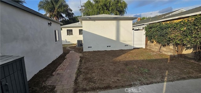 view of side of property featuring crawl space, fence, central AC unit, and stucco siding