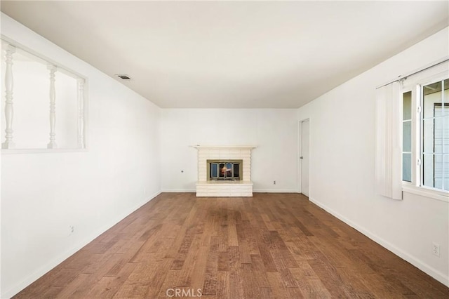 unfurnished living room featuring a fireplace, wood finished floors, visible vents, and baseboards