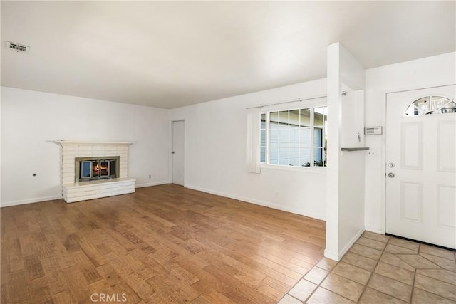 unfurnished living room featuring baseboards, a fireplace, visible vents, and wood finished floors