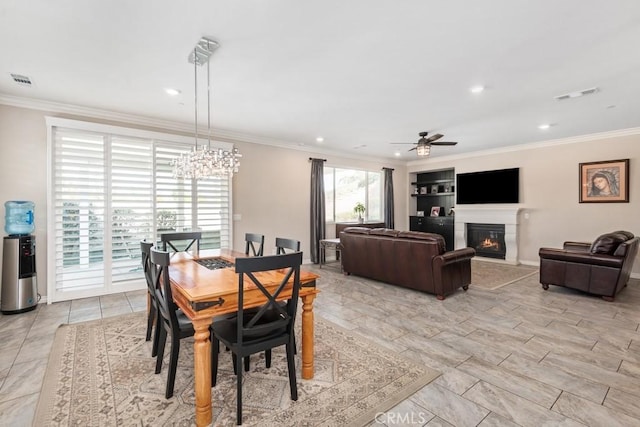 dining area featuring ceiling fan with notable chandelier, a glass covered fireplace, visible vents, and crown molding