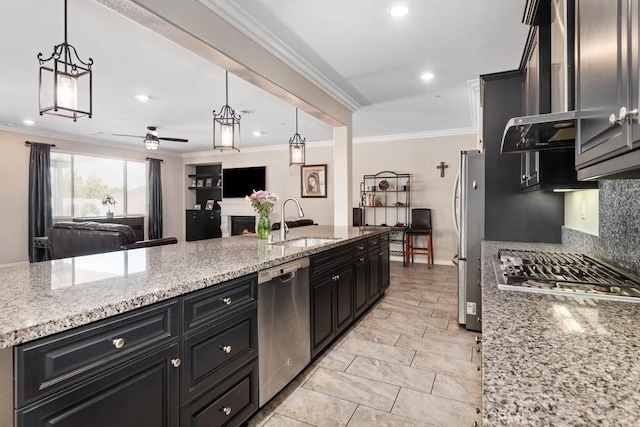 kitchen with stainless steel appliances, a sink, open floor plan, dark cabinetry, and crown molding