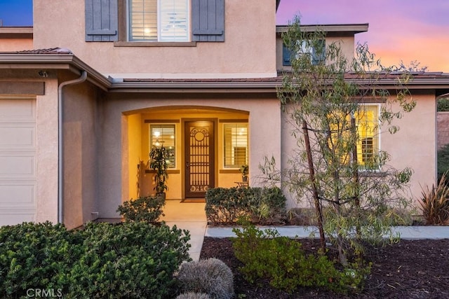 entrance to property featuring a garage, a porch, and stucco siding