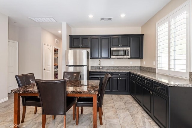 kitchen with appliances with stainless steel finishes, visible vents, a sink, and light stone counters