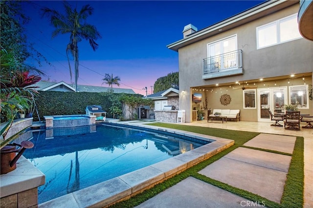 view of pool featuring a patio, a pool with connected hot tub, an outdoor kitchen, fence, and an outdoor living space