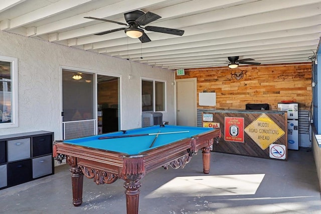 recreation room featuring concrete flooring, beam ceiling, a textured wall, and ceiling fan