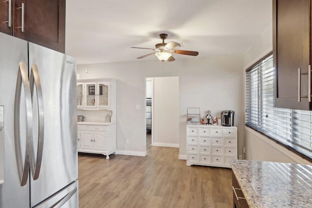 kitchen featuring light wood-type flooring, freestanding refrigerator, dark brown cabinetry, and light stone countertops