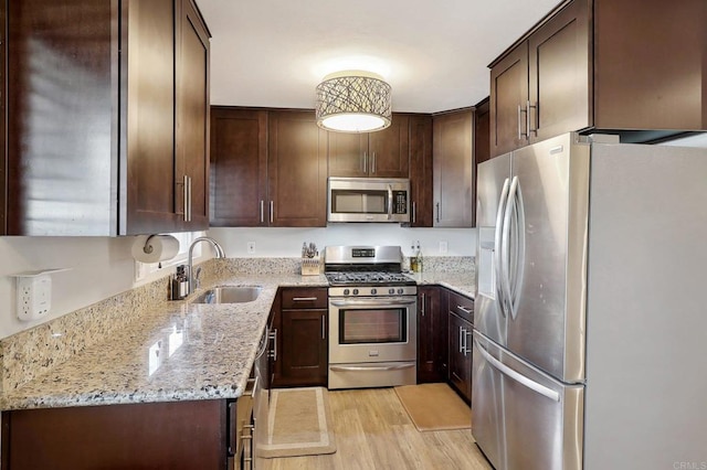 kitchen with light stone countertops, stainless steel appliances, dark brown cabinets, light wood-style floors, and a sink