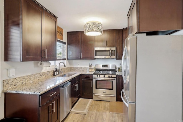 kitchen featuring dark brown cabinetry, stainless steel appliances, a sink, light wood-style floors, and light stone countertops