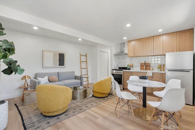 kitchen featuring appliances with stainless steel finishes, light wood-style flooring, wall chimney range hood, and tasteful backsplash