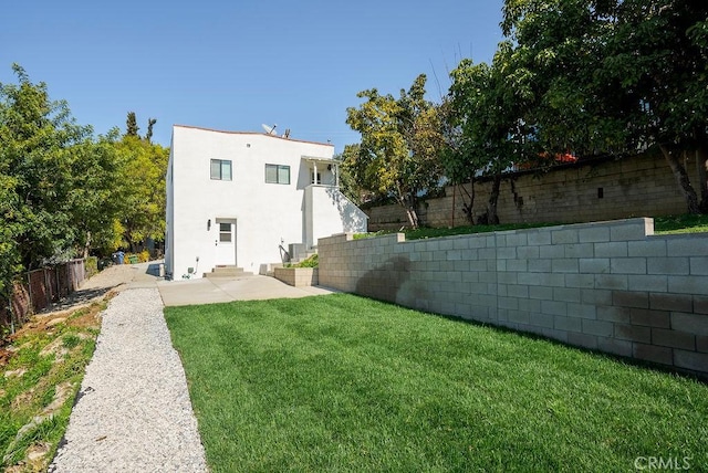 rear view of house featuring entry steps, a fenced backyard, a yard, a patio area, and stucco siding