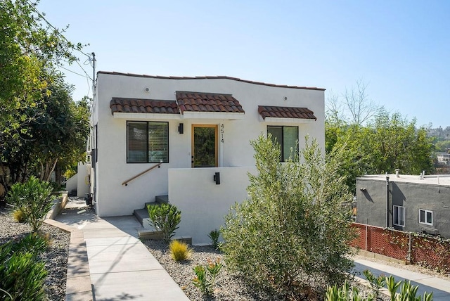 contemporary house featuring a tiled roof, fence, and stucco siding