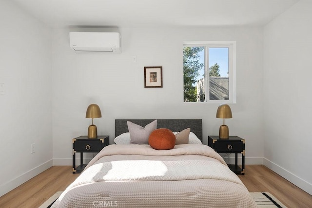 bedroom featuring light wood-type flooring, baseboards, and an AC wall unit