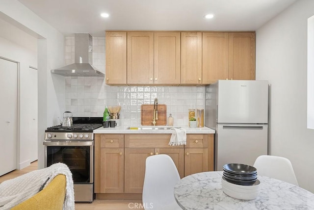 kitchen with light countertops, freestanding refrigerator, a sink, stainless steel gas range oven, and wall chimney exhaust hood