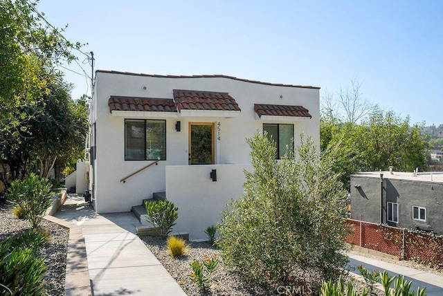 contemporary home with stucco siding, a tile roof, and fence