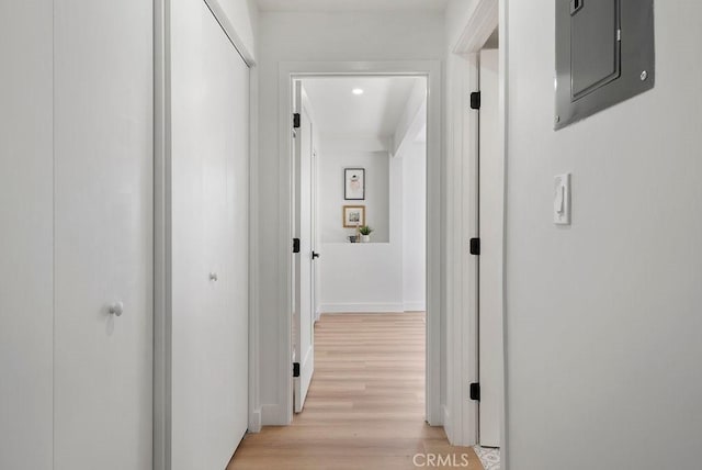 corridor with light wood-type flooring, electric panel, and baseboards