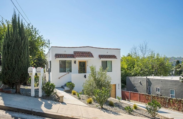 modern home with a tiled roof, fence, and stucco siding