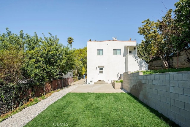 rear view of property featuring entry steps, a patio, a fenced backyard, a lawn, and stucco siding