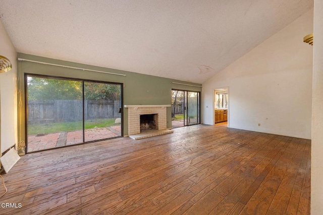 unfurnished living room with plenty of natural light, high vaulted ceiling, wood-type flooring, and a brick fireplace