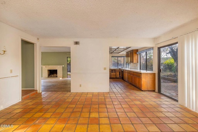 kitchen featuring brown cabinets, a fireplace, light countertops, visible vents, and a textured ceiling