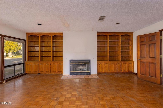 unfurnished living room with a textured ceiling, built in shelves, a fireplace with flush hearth, and visible vents